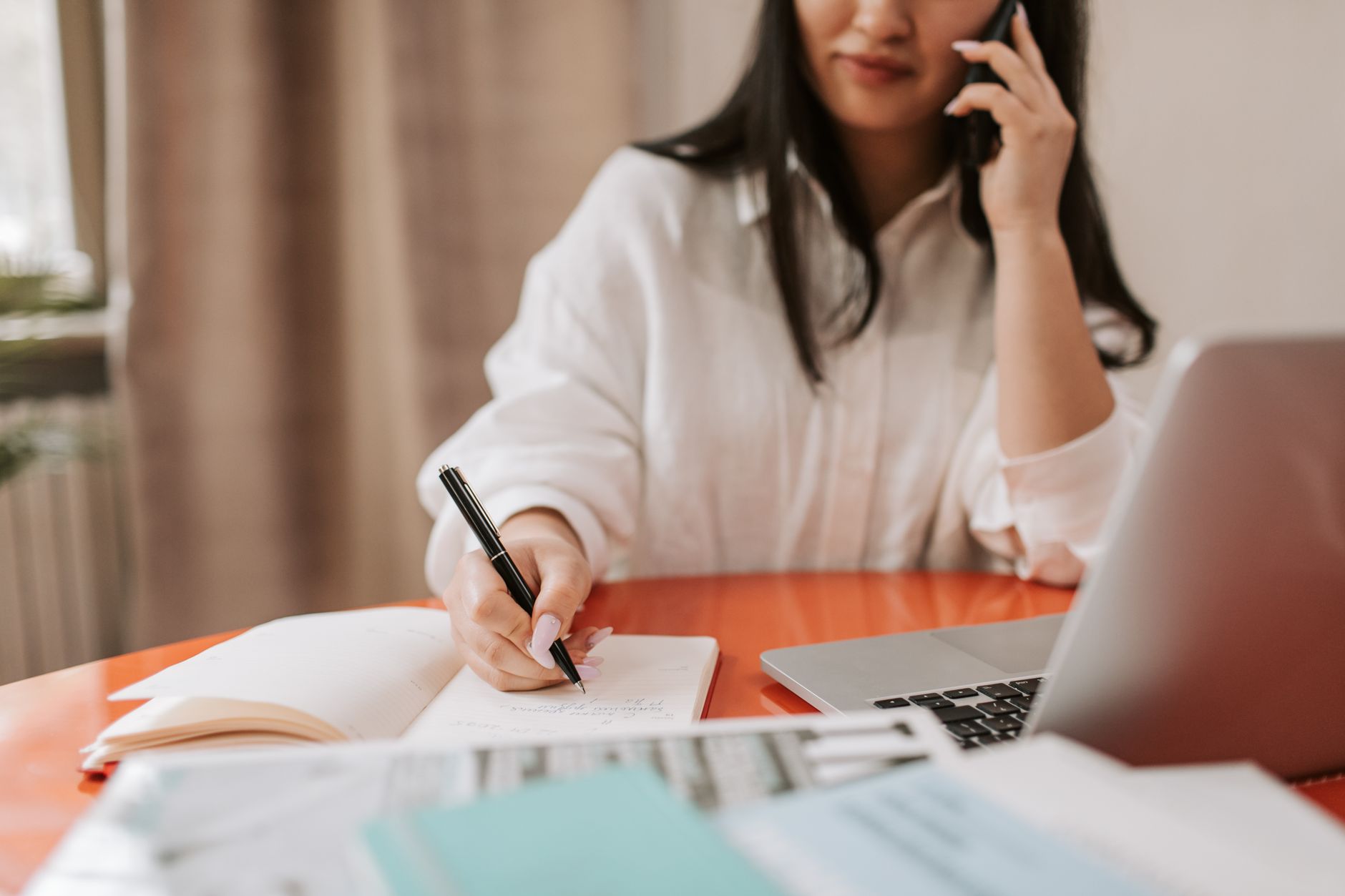 Een vrouw maakt aantekeningen terwijl ze aan de telefoon zit