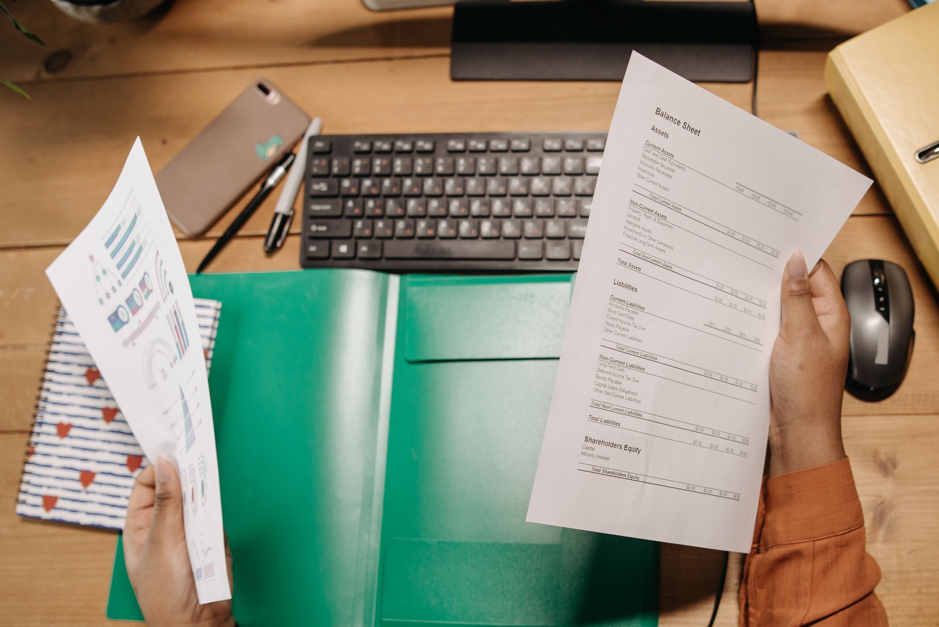 Handen bekijken overzichten op papier boven een bureau met toetsenbord