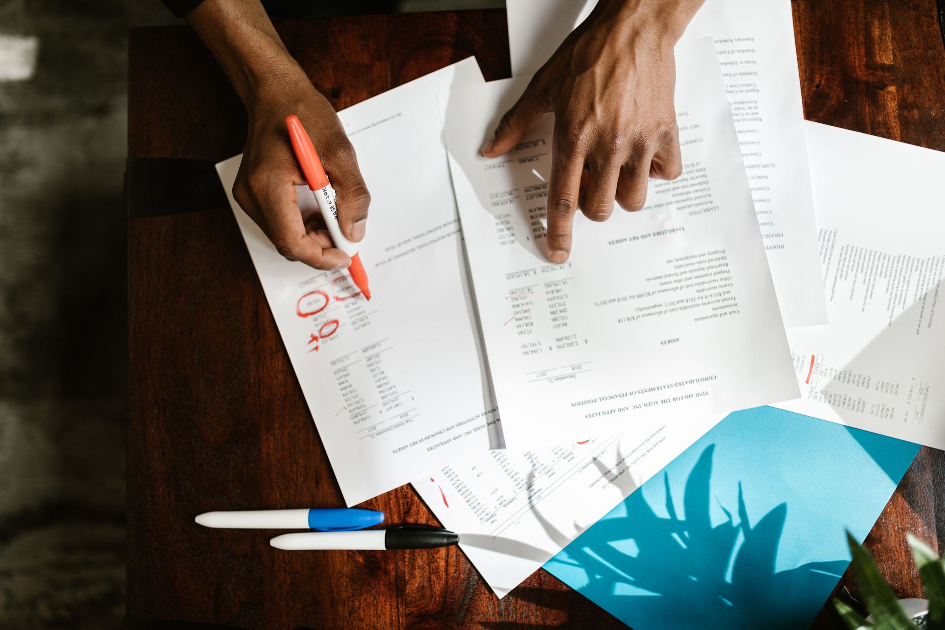 Twee handen markeren regels in financiële documenten op een bureau