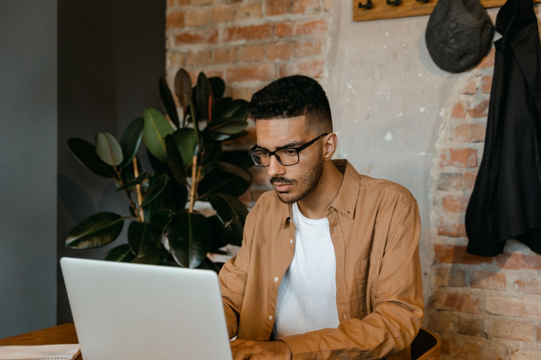 Een man met een bril werkt op een laptop in een café met bakstenen muur