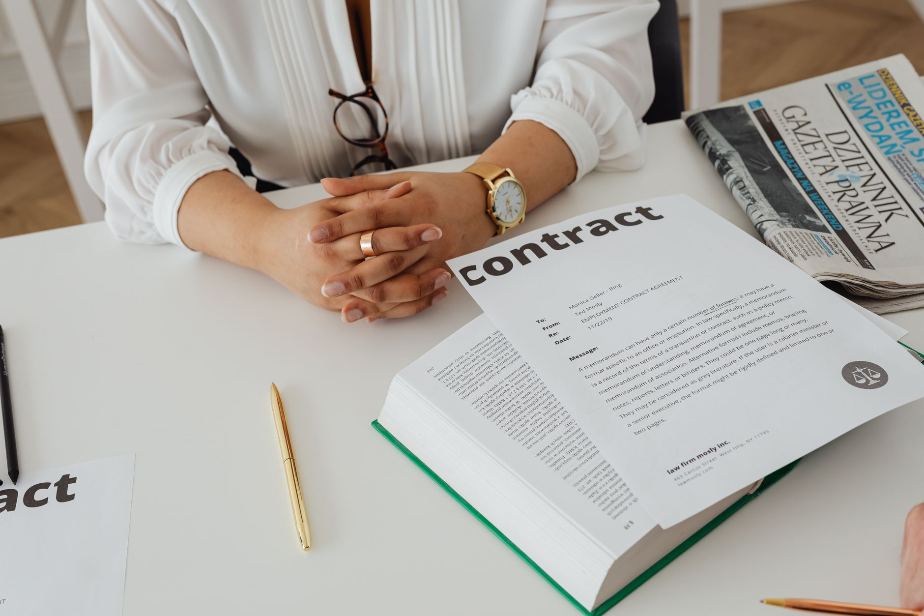 Vrouw met gevouwen handen aan bureau met contract, pen en boeken