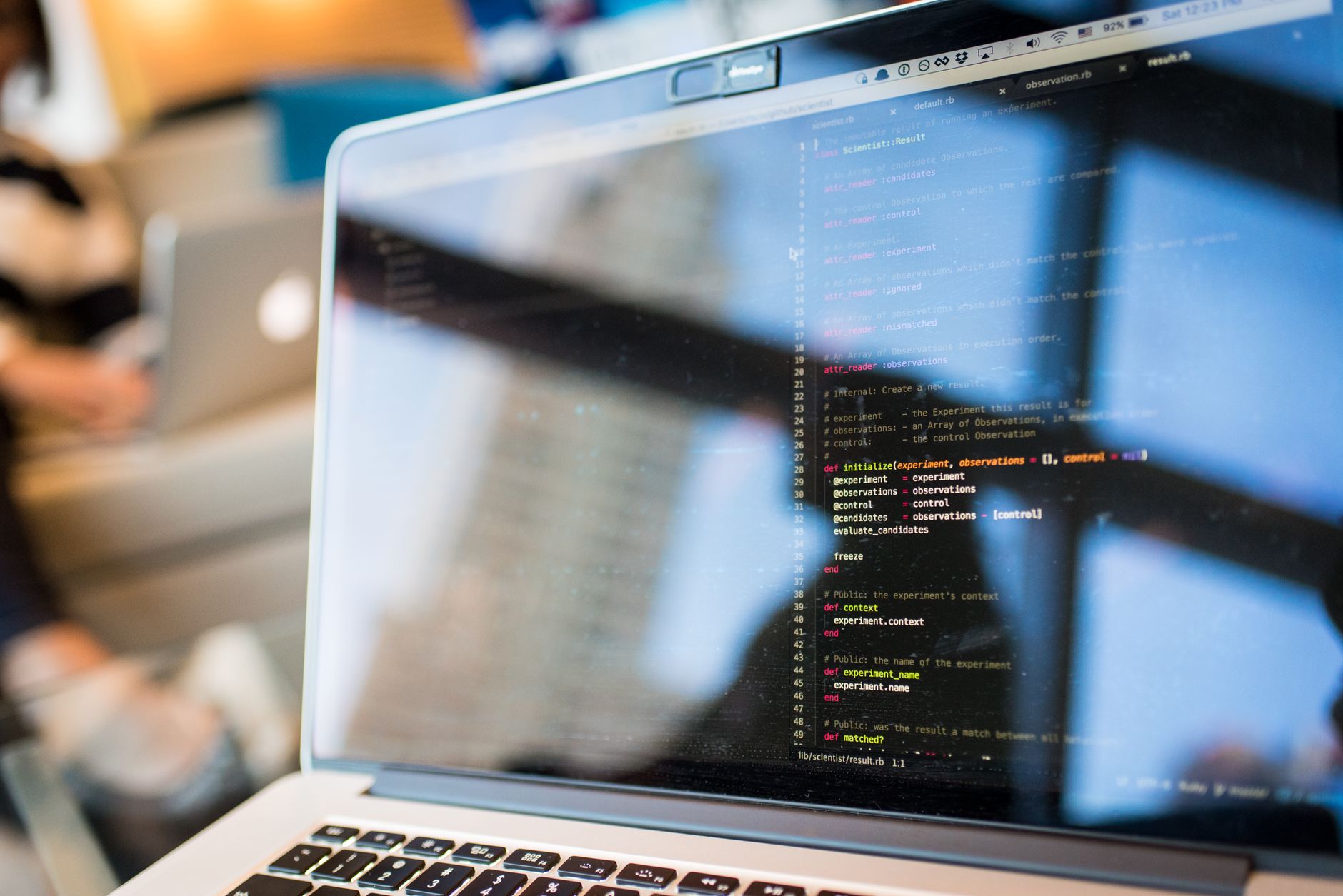 Laptopscherm met programmeercode, weerspiegeling van kantoorruimte zichtbaar in het display